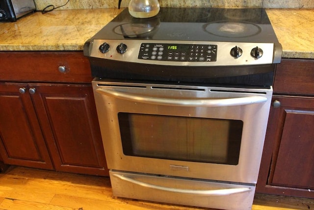 interior details featuring light wood-style floors, stainless steel range with electric stovetop, and light stone counters