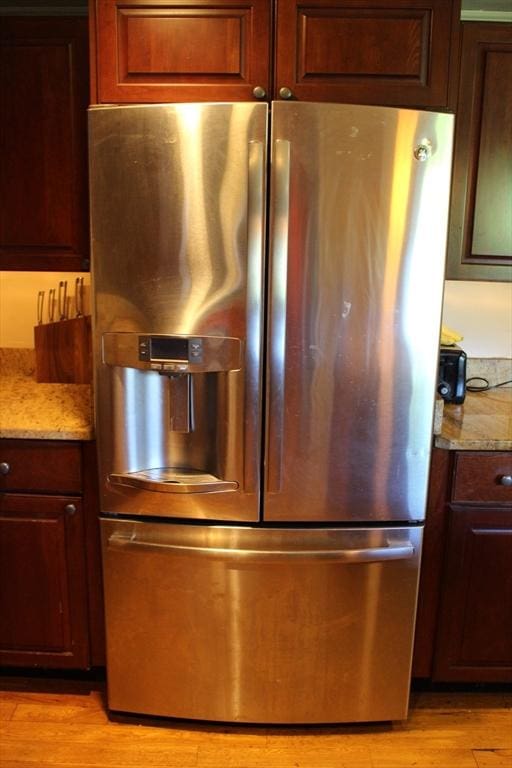 details with stainless steel refrigerator with ice dispenser, light stone countertops, and light wood finished floors