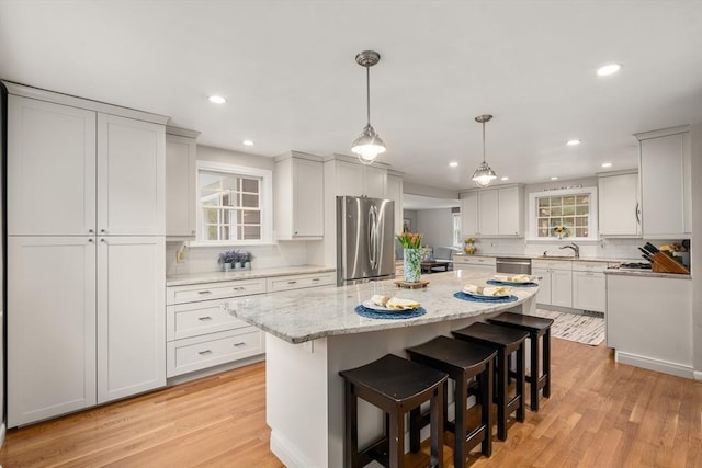 kitchen with stainless steel appliances, a kitchen island, backsplash, light hardwood / wood-style floors, and white cabinets