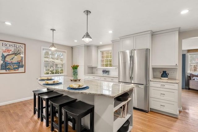 kitchen featuring a center island, stainless steel fridge, decorative light fixtures, decorative backsplash, and white cabinets