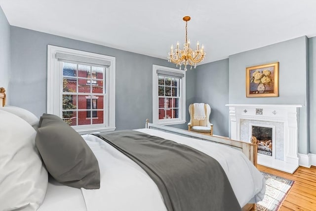 bedroom with a premium fireplace, a chandelier, and wood-type flooring