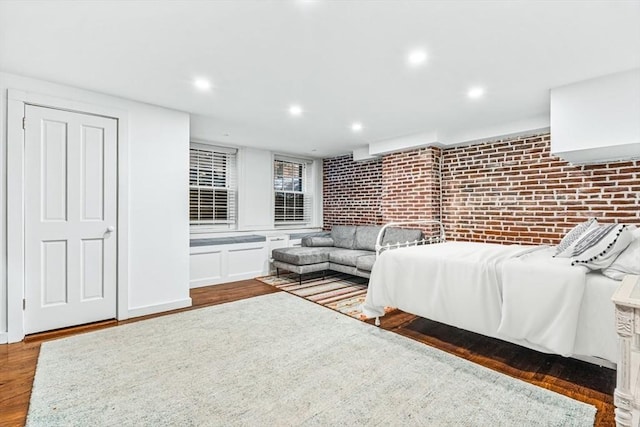 bedroom with dark hardwood / wood-style floors and brick wall