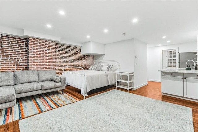 unfurnished bedroom with brick wall, light wood-type flooring, and stainless steel refrigerator