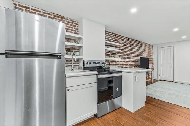 kitchen featuring white cabinets, brick wall, light wood-type flooring, and appliances with stainless steel finishes