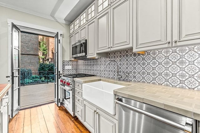 kitchen with backsplash, sink, crown molding, appliances with stainless steel finishes, and tile counters