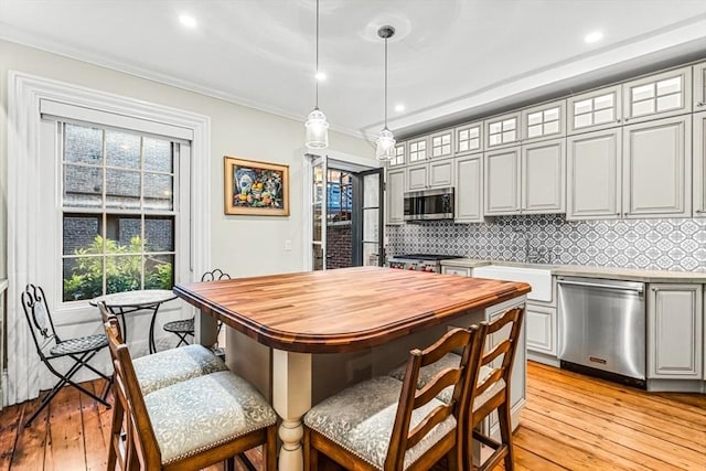 kitchen with pendant lighting, crown molding, light wood-type flooring, tasteful backsplash, and stainless steel appliances