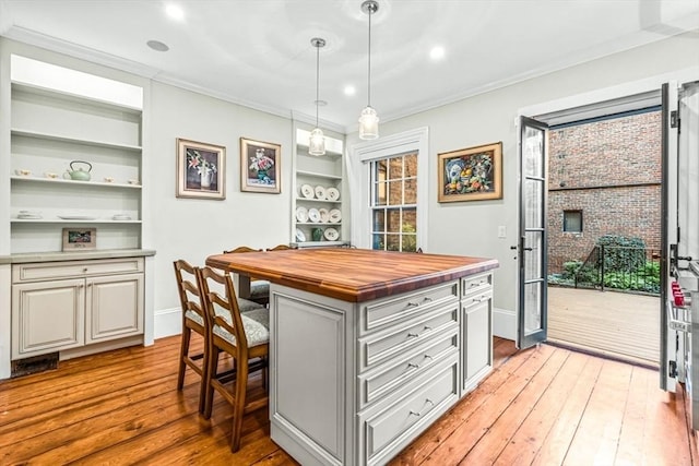 kitchen featuring crown molding, decorative light fixtures, butcher block countertops, a kitchen island, and a breakfast bar area