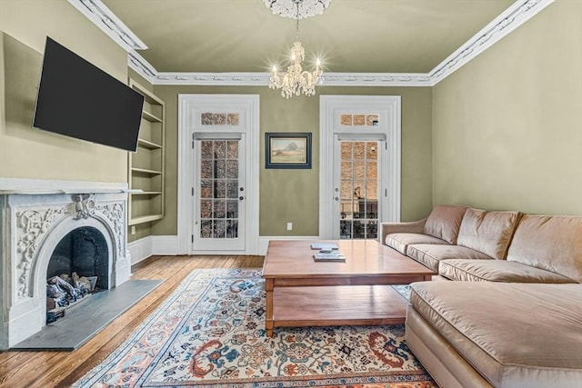 living room featuring light wood-type flooring, built in features, a fireplace, ornamental molding, and a notable chandelier