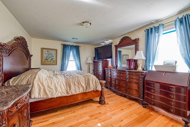 bedroom featuring light hardwood / wood-style flooring, multiple windows, and a textured ceiling