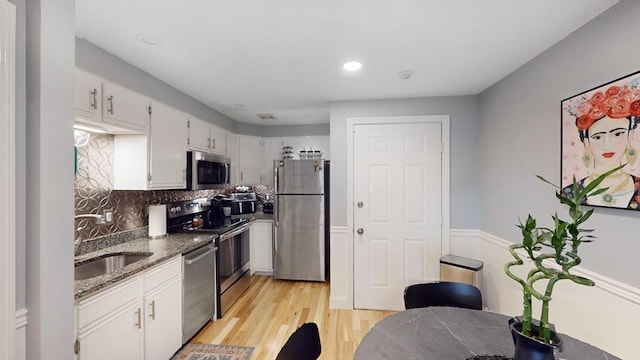 kitchen featuring stone counters, a sink, light wood-style floors, appliances with stainless steel finishes, and backsplash