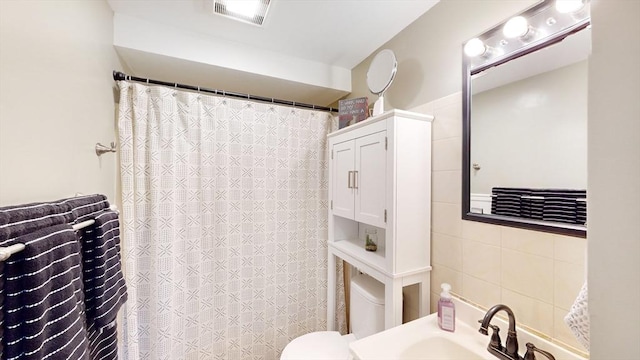 bathroom featuring visible vents, toilet, a sink, a shower with shower curtain, and tile walls