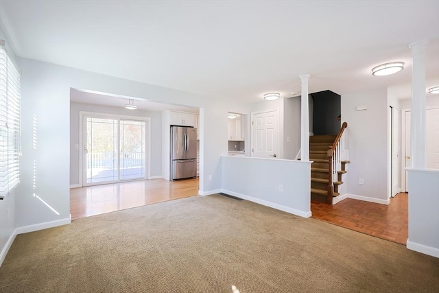 unfurnished living room featuring baseboards, stairway, light colored carpet, and ornate columns