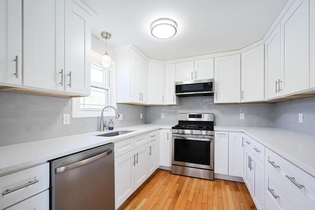 kitchen featuring light wood finished floors, white cabinets, appliances with stainless steel finishes, light countertops, and a sink