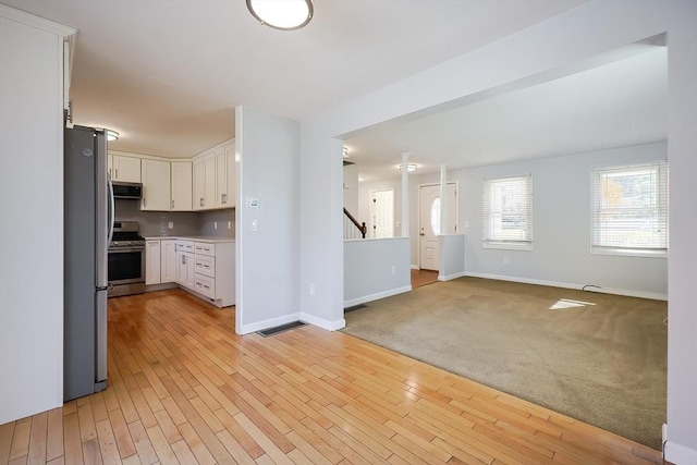 kitchen with light wood finished floors, white cabinetry, stainless steel appliances, and light countertops