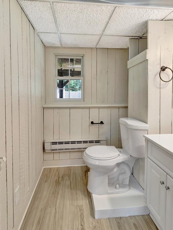4 Gary Rd, Norton, MA 02766 - bathroom with a baseboard heating unit, wood finished floors, vanity, wooden walls, and a drop ceiling