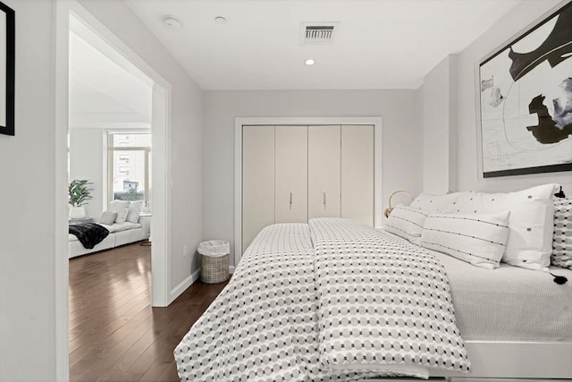 bedroom with baseboards, visible vents, dark wood finished floors, and a closet