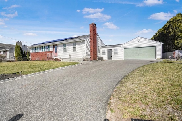 ranch-style home with roof mounted solar panels, a chimney, a detached garage, and a front lawn