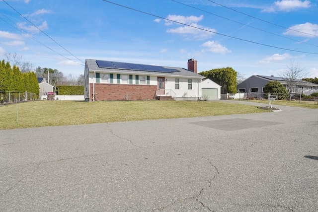 view of front of property featuring solar panels, a front lawn, fence, a garage, and an outbuilding