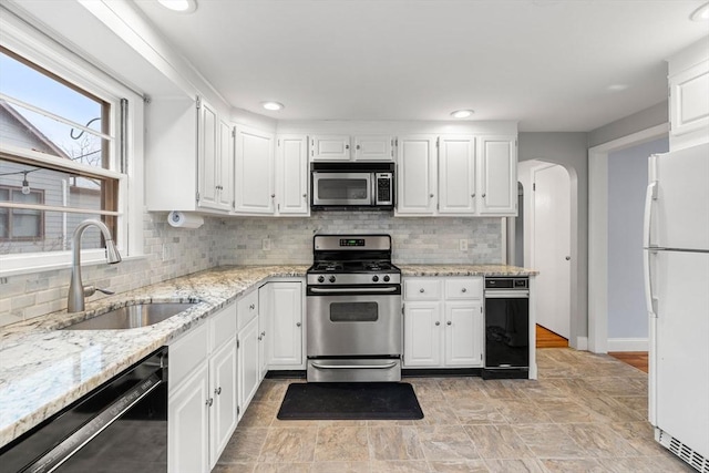 kitchen with white cabinets, arched walkways, stainless steel appliances, and a sink