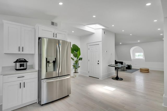 kitchen featuring white cabinets, lofted ceiling, light wood-type flooring, and stainless steel refrigerator with ice dispenser