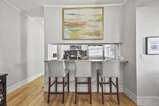 interior space with a breakfast bar area, wood finished floors, a sink, a peninsula, and stainless steel appliances