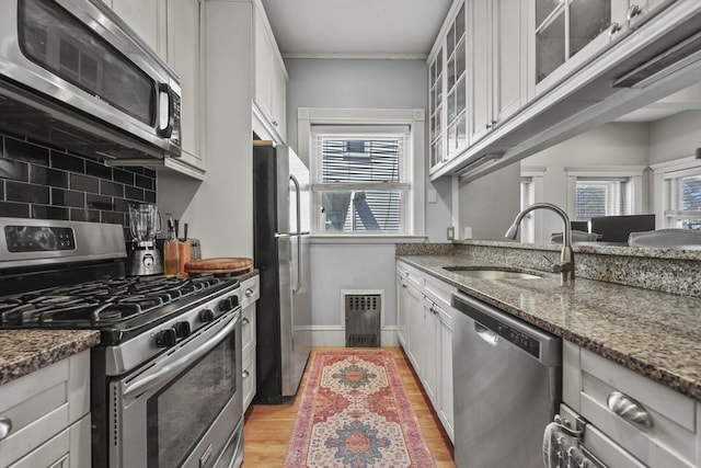 kitchen with backsplash, visible vents, appliances with stainless steel finishes, a sink, and dark stone countertops