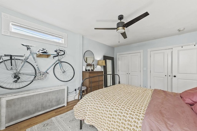 bedroom featuring radiator, wood finished floors, two closets, baseboards, and a ceiling fan