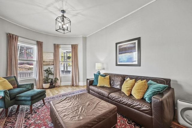 living area featuring baseboards, a notable chandelier, ornamental molding, and light wood finished floors