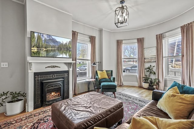 living room with crown molding, a chandelier, a glass covered fireplace, baseboards, and wood finished floors