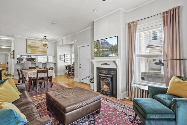 living room featuring a tiled fireplace, wood finished floors, baseboards, a notable chandelier, and ornamental molding