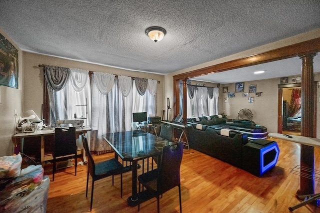 dining area featuring wood-type flooring, a textured ceiling, and decorative columns