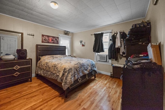 bedroom with cooling unit, light wood-type flooring, ornamental molding, and radiator