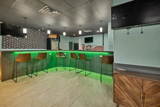 bar featuring black refrigerator, light tile patterned floors, a paneled ceiling, and hanging light fixtures