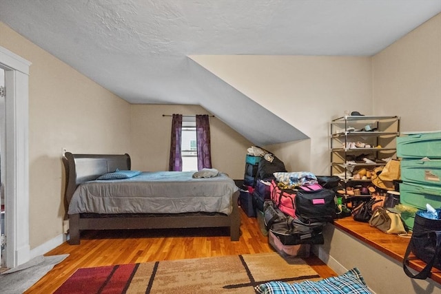 bedroom with a textured ceiling, light hardwood / wood-style flooring, and lofted ceiling