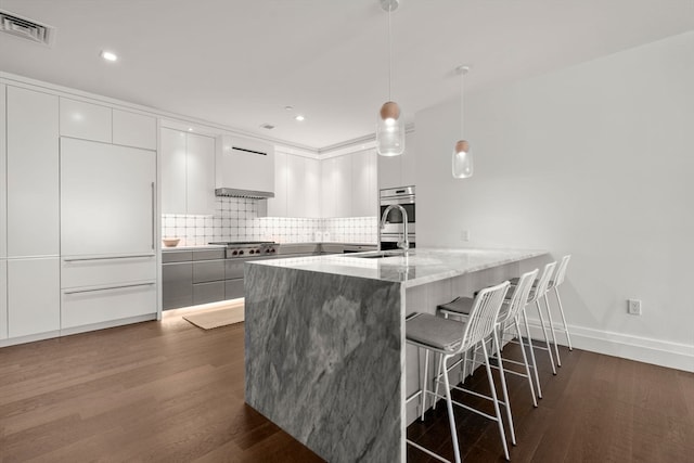 kitchen featuring sink, light stone counters, decorative backsplash, white cabinetry, and dark wood-type flooring