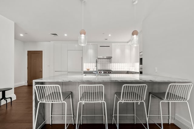 kitchen with a breakfast bar, dark hardwood / wood-style flooring, white cabinets, and tasteful backsplash