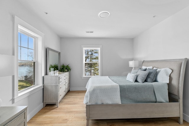 bedroom with multiple windows, a water view, and light wood-type flooring