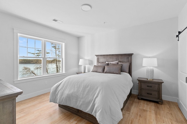 bedroom featuring a barn door and light hardwood / wood-style floors