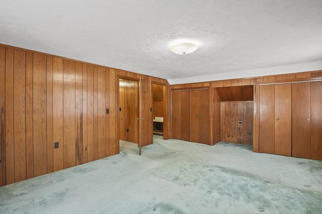 unfurnished bedroom featuring wooden walls, a textured ceiling, two closets, and carpet floors