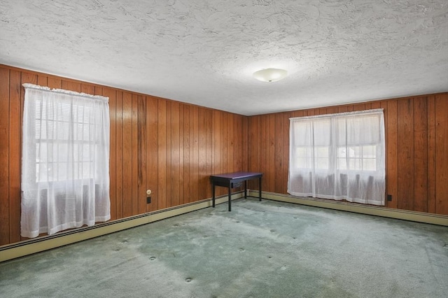 carpeted spare room featuring a baseboard radiator, a textured ceiling, and wood walls