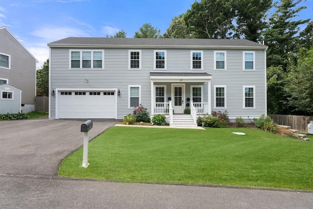 colonial house featuring aphalt driveway, covered porch, an attached garage, a front yard, and fence