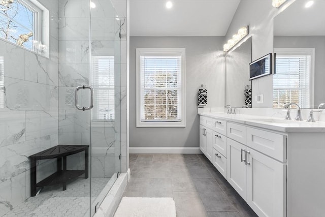 full bath with double vanity, a sink, a marble finish shower, and baseboards