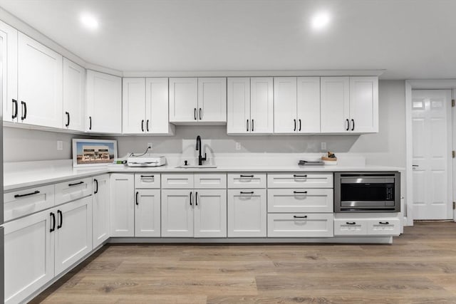 kitchen with stainless steel microwave, light wood-type flooring, a sink, and white cabinets