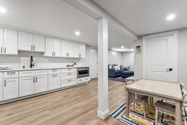 kitchen featuring light countertops, stainless steel microwave, light wood-style floors, white cabinetry, and a sink