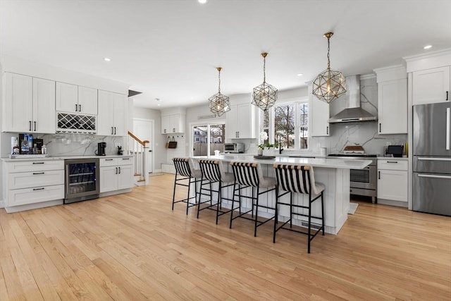 kitchen featuring wine cooler, stainless steel appliances, a breakfast bar, light wood-style floors, and wall chimney exhaust hood