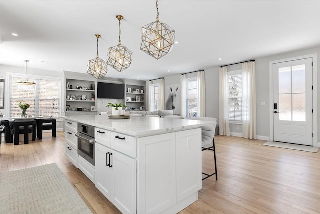 kitchen featuring light wood-style flooring, stainless steel oven, white cabinetry, hanging light fixtures, and a center island