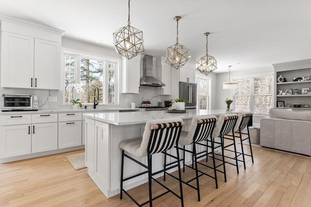 kitchen featuring light wood finished floors, a toaster, light countertops, wall chimney range hood, and high end fridge