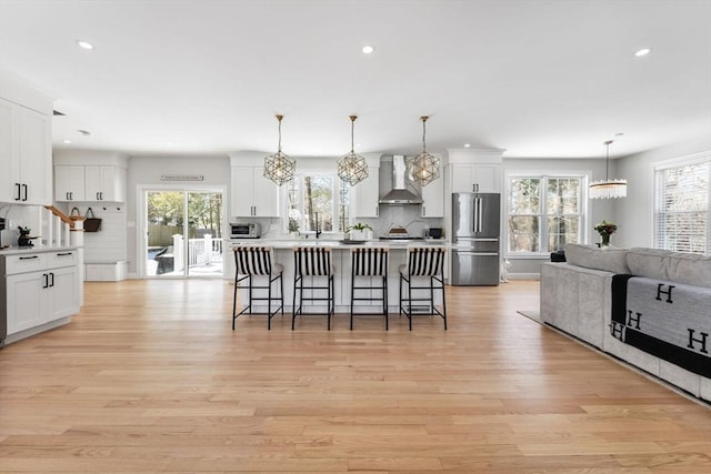 kitchen featuring appliances with stainless steel finishes, a kitchen breakfast bar, light wood-type flooring, wall chimney range hood, and white cabinetry