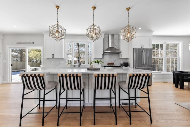 kitchen with a kitchen island, white cabinetry, light countertops, backsplash, and wall chimney exhaust hood