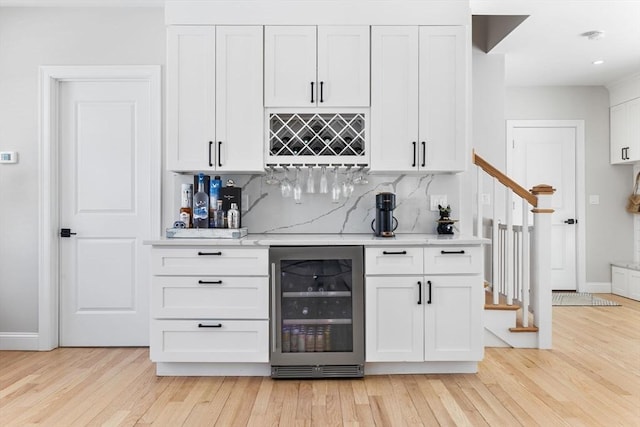 bar with a bar, light wood-type flooring, beverage cooler, and tasteful backsplash